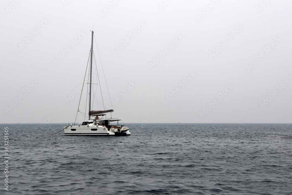 White single-masted yacht with a deflated sails in the open sea. Seascape in storm weather, travel and vacation concept