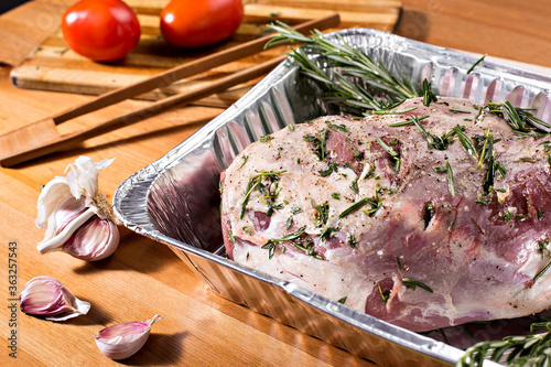 Raw meat in an aluminum dish on a wooden table against a background of rustic utensils
