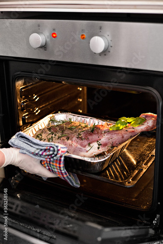 Meat steak baked in foil with fresh herbs and vegetables.  Woman's hand gets out of the oven. 
oven-cooked meat