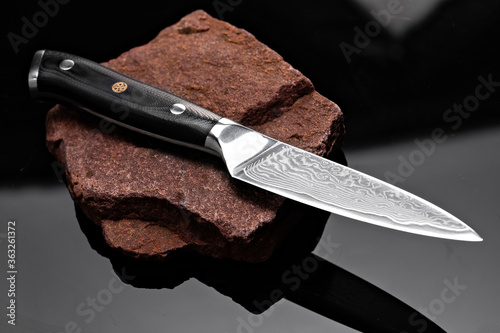 A large kitchen knife with a black handle on a dark background. Knife with a wide sharp blade. Scratched steel surface of the knife blade. photo