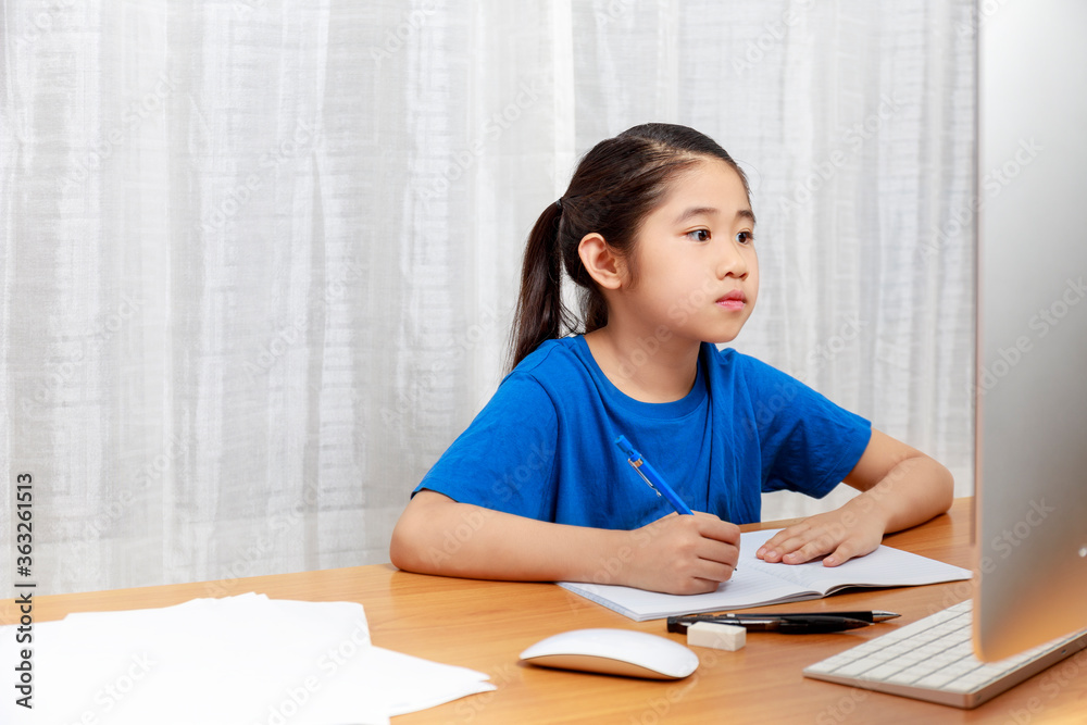 Asian little girl is studying online via the internet sitting and writing in living room at home. Asia children writeing with pencil on notebook. online learning at home or learn frome home concept. Asian little girl is studying online via the internet sitting and writing in living room at home. Asia children writeing with pencil on notebook. online learning at home or learn frome home concept.