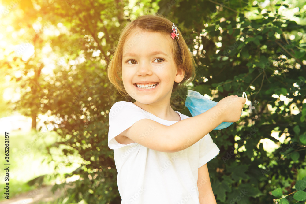 Little cute girl take off medical face mask with happy smile in the outdoor, close up. Concept of happy end and victory over coronavirus. Little cute girl take off medical face mask with happy smile in the outdoor, close up. Concept of happy end and victory over coronavirus.