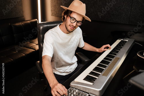 Young musician composing new song on midi piano in sound recording studio. Attractive guy playing on electric piano in studio photo