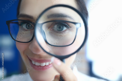 Woman with glasses looks through magnifying glass and smiles. Research and analysis of modern market startup startup concept