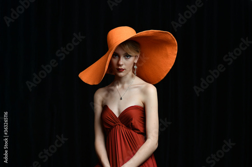 beautiful girl in a wide-brimmed hat and in a burgundy evening dress posing on a black background