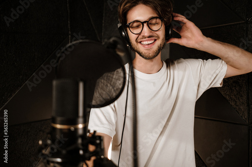 Young attractive male singer in headphones joyfully singing in sound studio photo