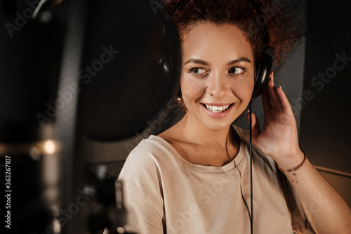 Portrait of beautiful singer listening sound in headphones working on new music album in recording studio photo