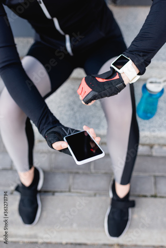 cropped view of sportswoman with fitness tracker on hand holding smartphone with blank screen