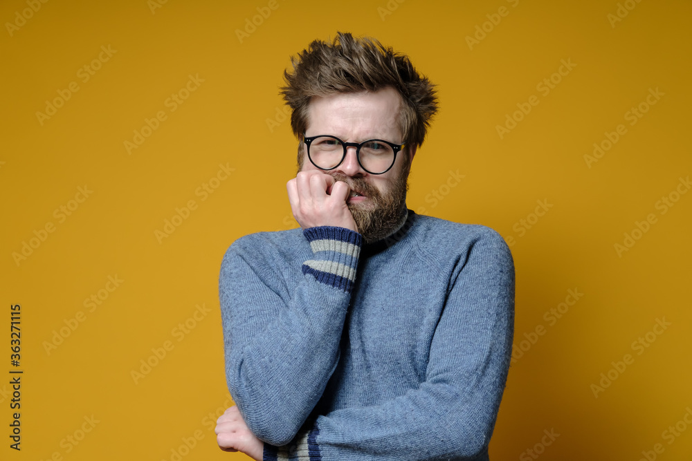 Frowned, agitated man nervously bites his nails and looks thoughtfully with alarm. Frowned, agitated man nervously bites his nails and looks thoughtfully with alarm.