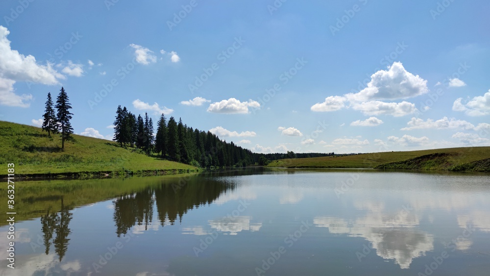 reflection of trees and clouds on the surface of the lake water on a sunny day