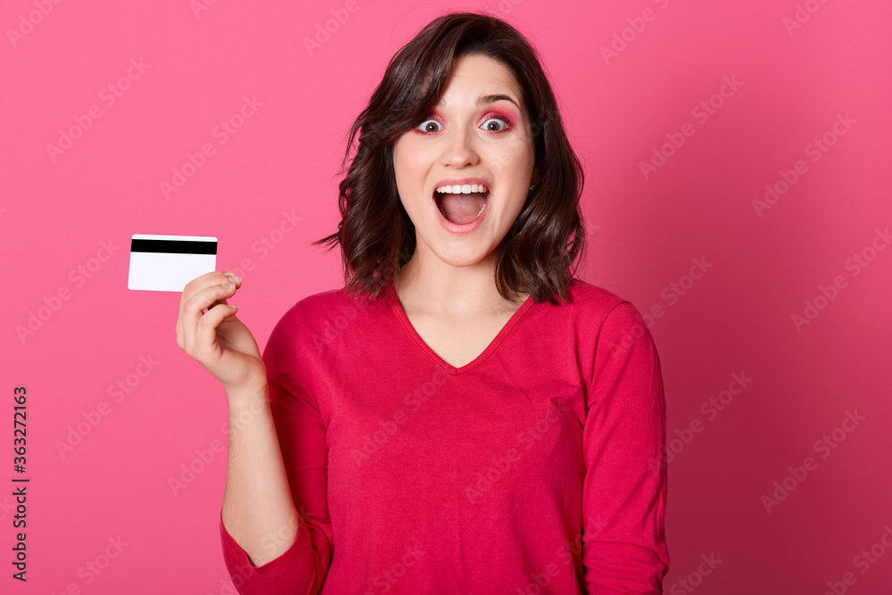 Happy astonished woman with credit card in hand, looking directly at camera with widely opened mouth and big eyes, brunette female win big sum of money. Happy astonished woman with credit card in hand, looking directly at camera with widely opened mouth and big eyes, brunette female win big sum of money.