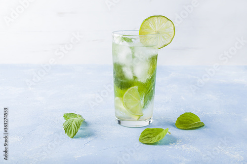 Refreshing cool detox drink with lime and mint on blue background. Summer lemonade or ice tea in a glass. Mojito cocktail with ice cubes. Healthy eating. Сopy space for text