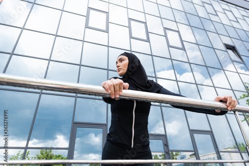 low angle view of arabian woman in hijab holding handrail while standing near modern building