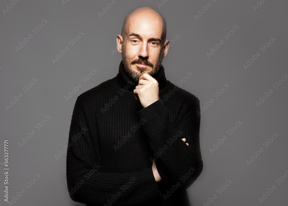 Fashion Portrait of a 40-year-old man standing over a light gray background in a black sweater. Close up. Classic style. Bald shaved head. Copy-space. Studio shot