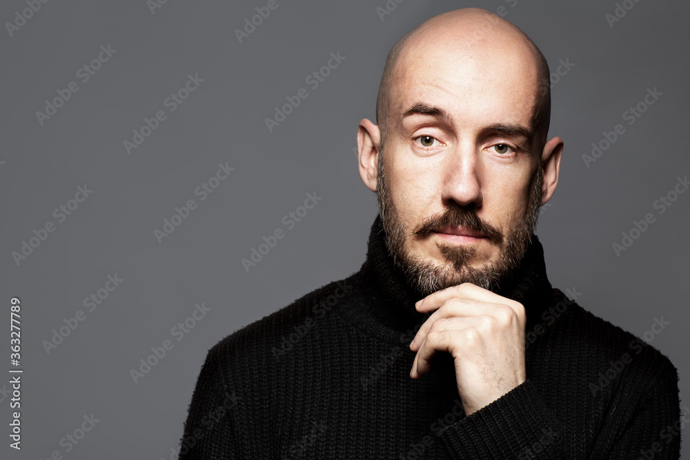 Fashion Portrait of a 40-year-old man standing over a light gray background in a black sweater. Close up. Classic style. Bald shaved head. Copy-space. Studio shot Fashion Portrait of a 40-year-old man standing over a light gray background in a black sweater. Close up. Classic style. Bald shaved head. Copy-space. Studio shot