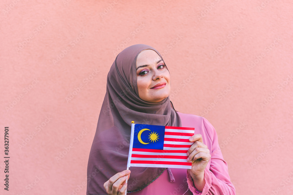 Muslim woman in hijab holds flag of  Malaysia