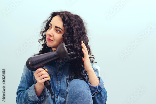 Woman using a modern hairdryer at home. Woman makes herself curly hairstyle. Beauty and haircare concept. photo