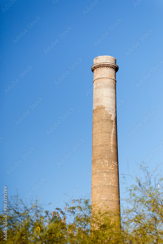 Vertical view of restored «La Ramona» smokestack, built in 1890 in historic mining village -now industrial ruin- of El Triunfo, Baja California Sur, Mexico. Old chimney against blue sky background