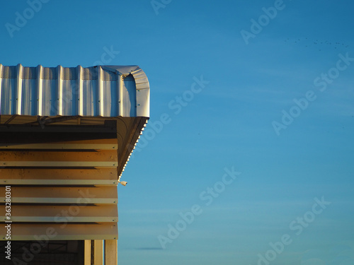 The metal sheet roof of the factory receives sunlight from the morning sun. On a background that is blue sky.