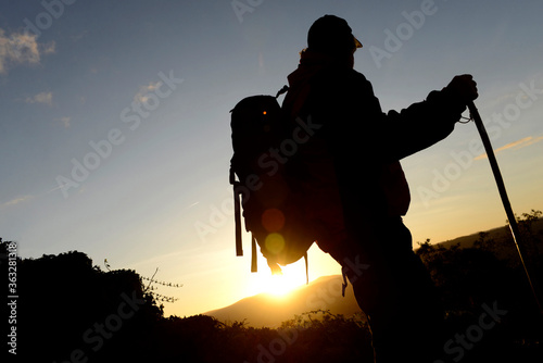 Silhouette of older man with backpack and walking stick watching the sunset in the middle of nature