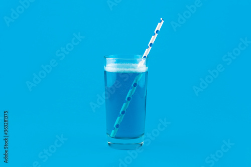 Blue lemonade with gas bubbles and a cocktail straw isolated on blue background