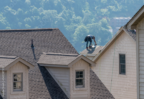 Young roofing contractor replacing the old shingles on a townhouse roof high above the ground