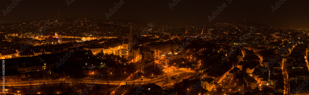 Panoramic aerial drone shot of Fisherman Bastion with lights on on Buda Hill in Budapest evening