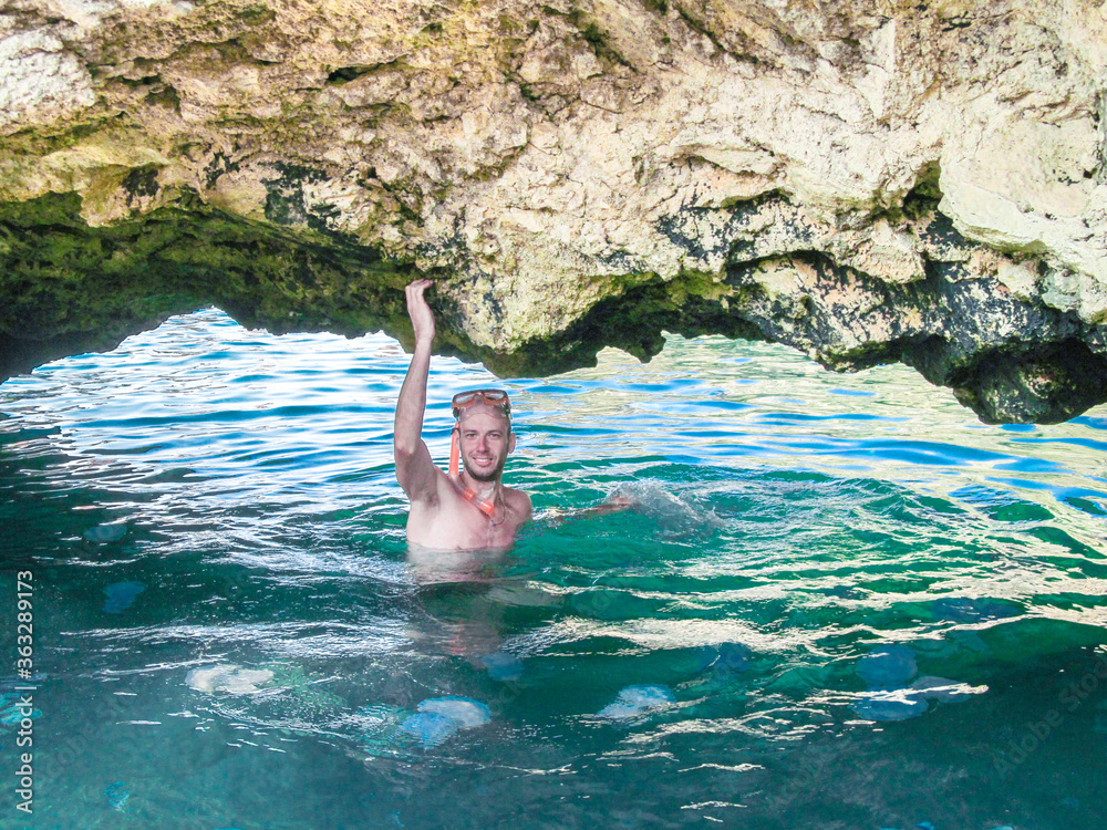 The guy in the mask for swimming is near the entrance to the underwater cave.A man swims in the sea with jellyfish. A swimmer holds his hand by the rock.