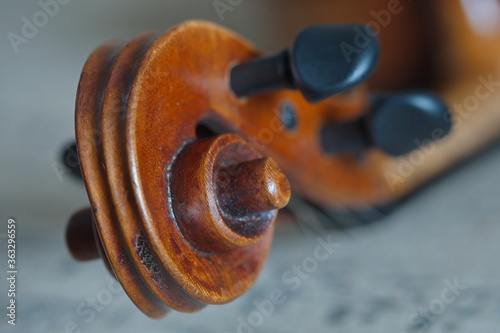 Wallpaper Mural Eine braune Geigen Schnecke aus Holz mit zwei schwarzen Stimmwirbeln liegend auf eine Stoff Decke mit Musik Noten Druck drauf. Torontodigital.ca