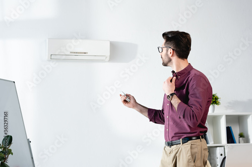 young businessman suffering from heat, touching shirt and switching on air conditioner with remote controller © LIGHTFIELD STUDIOS