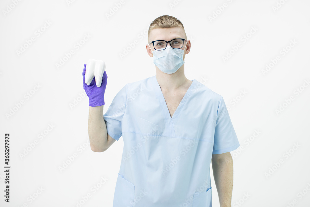 young handsome intern doctor wearing glasses and protective mask holds model of molar tooth looking at camera isolated on white background. Concept of Dental Surgery. Dental care concept