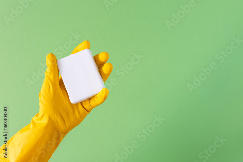 Hand in a yellow rubber glove with soap on a green background