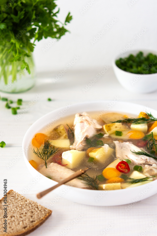 Chicken soup with fresh vegetables, chicken wings broth and young potatoes with onions and carrots, chopped green onions and parsley