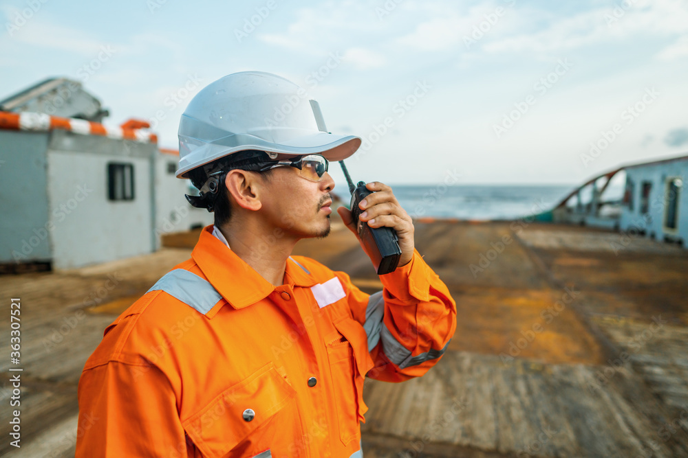 Filipino deck Officer on deck of vessel or ship , wearing PPE personal protective equipment. He holds VHF walkie-talkie radio in hands. Dream work at sea Filipino deck Officer on deck of vessel or ship , wearing PPE personal protective equipment. He holds VHF walkie-talkie radio in hands. Dream work at sea