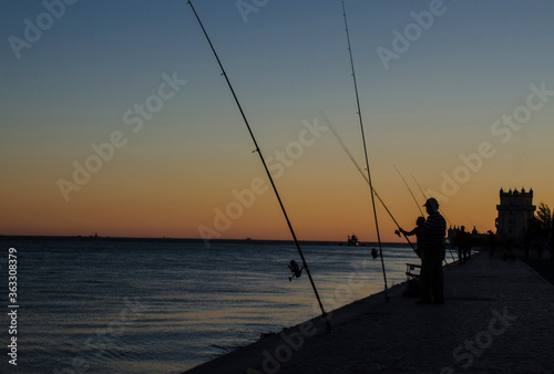 Fishermen silhouette at sunset near Belem tower, in Lisbon, Portugal