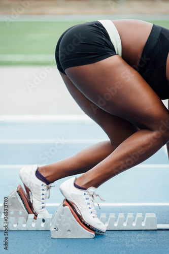 Unrecognizable afro sportswoman in sportswear beginning race from crouch start position on starting blocks