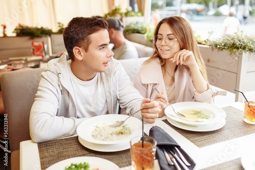 A cheerful and beautiful couple are relaxing on a summer terrace in a restaurant with food and drinks. The guy and the girl have fun on the terrace