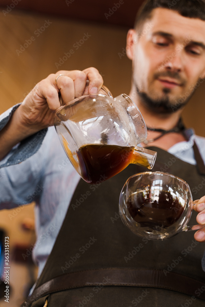 Close-up pouring coffee in double glass cup in cafe by handsome bearded barista. Coffee brewing syphon and aeropress alternative methods. Advert for social networks for cafe and restaurant.