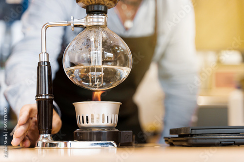 Syphon coffee brewing process. Close-up syphon is heating by fire. Barista looking at alternative coffee brewing process on the fire. Advert for social with empty right side for text of advertise