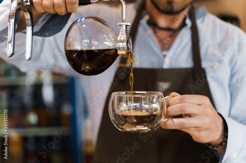 Close-up Syphon alternative method of making coffee. Barista pours hot coffee in syphon device for customers. Coffee brewing in cafe. Scandinavian method of coffee making.