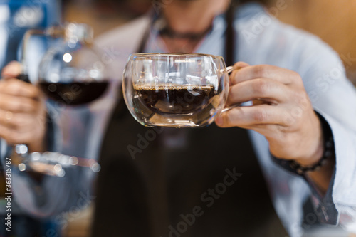 Syphon alternative method of making coffee. Barista gives hot coffee in double glass cup to customers. Coffee brewing in cafe. Scandinavian method of coffee making.