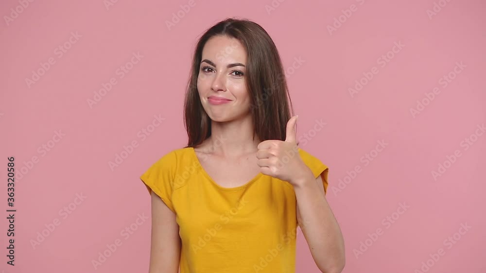 Smiling beautiful young woman girl 20s years old in yellow t-shirt posing isolated on pastel pink background studio. People lifestyle concept Look camera approvingly say wow it is ok showing thumbs up Smiling beautiful young woman girl 20s years old in yellow t-shirt posing isolated on pastel pink background studio. People lifestyle concept Look camera approvingly say wow it is ok showing thumbs up