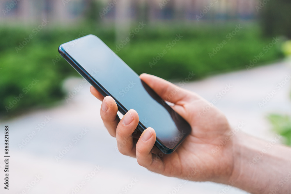 Close up cropped shot of male hand holding mobile phone outdoors