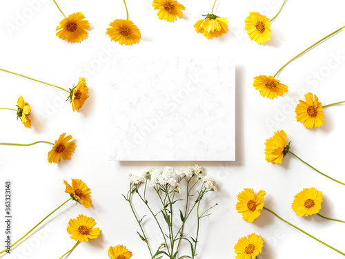 Flower composition. A template from a sheet of paper with a marble pattern is on a white background. Nearby are yellow flowers. Social media background. Holiday layout. Flat lay, copy space.