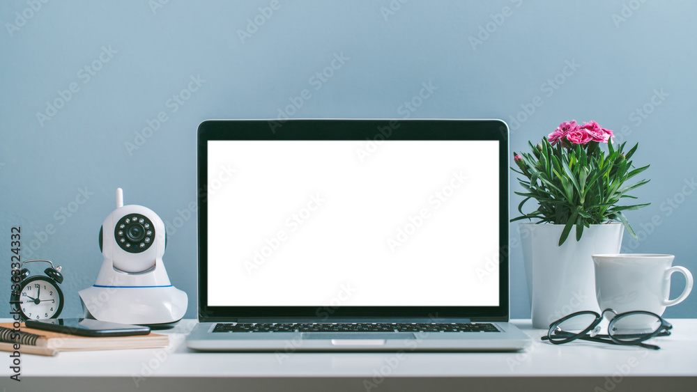 Front view of laptop with white blank screen standing at the office desk with flower pot, web-camera, coffee cup and office supplies Front view of laptop with white blank screen standing at the office desk with flower pot, web-camera, coffee cup and office supplies