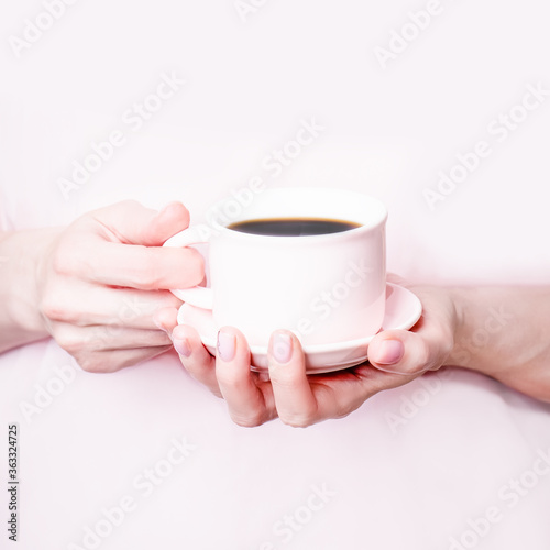 Female hands holding pink cup of black coffee on pink background. Copy space