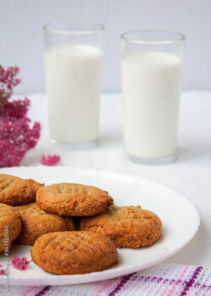 homemade peanut cookies with milk and pink flowers on the white background homemade peanut cookies with milk and pink flowers on the white background