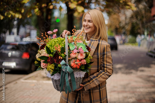 beautiful smiling woman in coat holds basket with flowers inside.