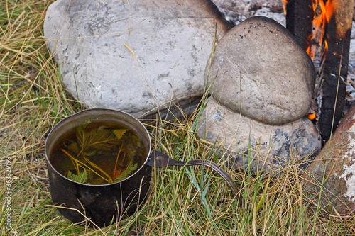 Bonfire and tourist bowler with herbal tea. Concept of tourist food on a hiking. Cooking on the fire