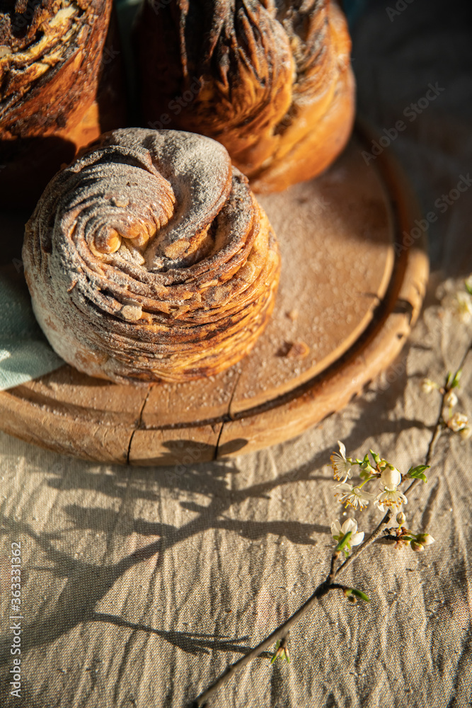 Homemade cruffin breads with dried fruits, cocoa and cinnamon fillings on wooden board and blooming cherry twig on linen tablecloth . Homemade cruffin breads with dried fruits, cocoa and cinnamon fillings on wooden board and blooming cherry twig on linen tablecloth .